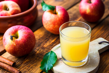 Frischer Apfelsaft in einem Glas und rote Äpfel auf einem braunen Holztisch. Nahaufnahme, Herbst.