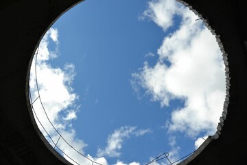 Blue sky with clouds through a round opening in the unfinished roof