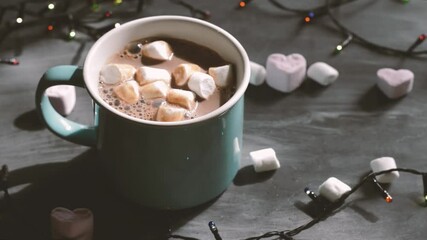 A mug with a hot drink, cocoa, hot chocolate or cappuccino with marshmallows. Women's hands put marshmallows in a cup.