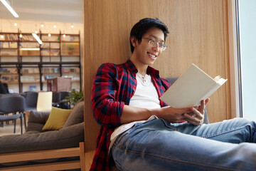 Asian smiling male student reading book in library