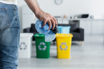 Cropped view of man holding plastic bags near blurred cans with recycle sign at home