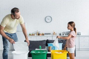 Father and daughter sorting garbage in trash cans with recycle sign in kitchen