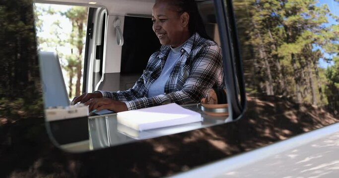 African senior woman using computer laptop inside camper mini van 