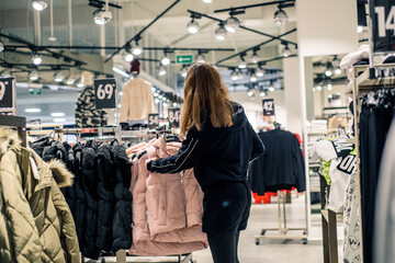 Girl in a clothing store. shopping and sales. Teenager chooses jacket or coat