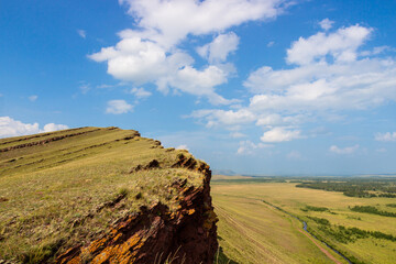 Perfect landscape from the edge of the cliff of the Sunduki mountain range on the summer green steppe under the blue sky in Khakassia, Russia