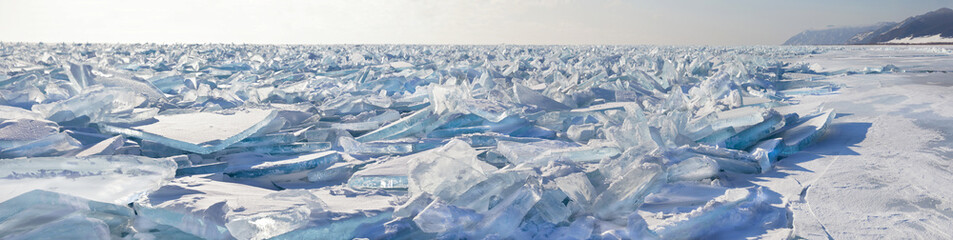 A panoramic view of the endless field of ice hummocks. Pieces of blue transparent ice on the frozen Lake Baikal on a frosty winter day. Natural cold background. Unusual winter landscape