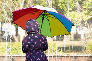 Back of child holding multicolor umbrella in sunny and rainy day