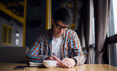 Young millennial male sitting at table studying. Caucasian student using netbook in coffee shop interior for write ideas. Man author creating article