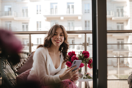 Tender Italian School Girl Chatting With Friends While Looking Into The Camera. Wearing Cozy Milky Cardigan And Light Singlet With Bright Red Lipstick, Posing In The Veranda With Daylight