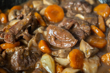 Close up Ready of Beef Burgeoning beef dish in a frying pan. meat, carrots and onions and mushrooms. Appetizing sauce. Slow food concept. Close-up