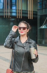 Beautiful young woman standing near modern city building with cup of coffee