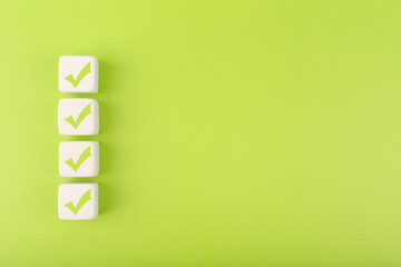 Four checkmarks on white cubes against bright green background with copy space. Concept of...