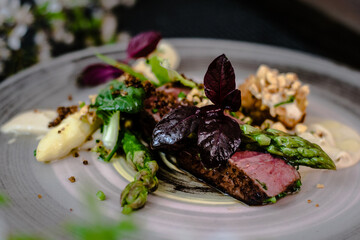 Dish of ostrich steak with white and green asparagus, garden greens and sauce on a plate on wooden table in a restaurant