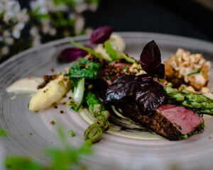 Dish of ostrich steak with white and green asparagus, garden greens and sauce on a plate on wooden table in a restaurant