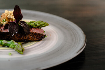 Dish of ostrich steak with white and green asparagus, garden greens and sauce on a plate on wooden table in a restaurant