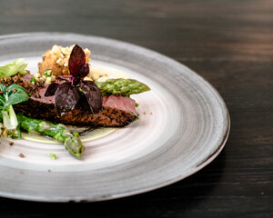 Dish of ostrich steak with white and green asparagus, garden greens and sauce on a plate on wooden table in a restaurant