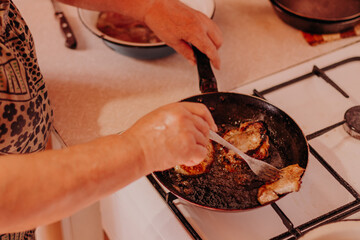 Frying pan with roasted steaks meat on fire at domestic kitchen. Old female turning meat.