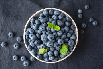Blueberries in bowl over black textile background, top view. Freshly picked summer berries