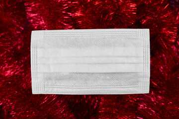 Flat lay festive christmas decoration and face medical protection mask on red tinsel background, Christmas and New year, goodbye 2020,  New normal year.