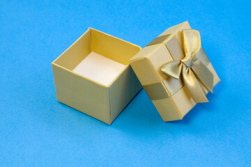 Empty golden gift box with silk gold ribbon bow on bright blue background