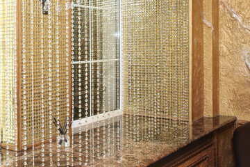 Window decorated with shiny curtains in the form of beads in a golden interior