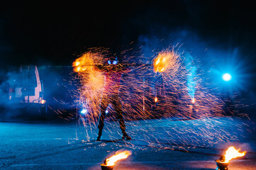 Fire show, dancing with flame, male master juggling with fireworks, performance outdoors, draws a fiery figure in the dark, bright sparks in the night. A man in a suit LED dances with fire.