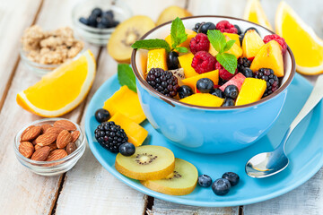 Concept of low calories delicious desserts. Summer fresh bowl with colorful fruit salad. Healthy natural organic food. Tasty sweet snack, light simple tasty lunch. Close up  wooden background