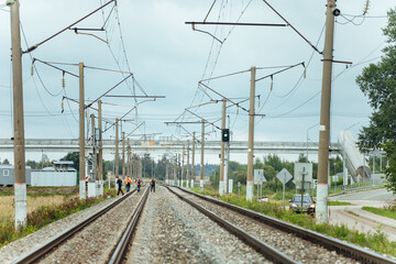 Fototapeta na wymiar workers in orange uniforms walk along the railway tracks. the repair team is going to work by rail. stone embankment of the railway and power lines. it is dangerous to walk on railway tracks