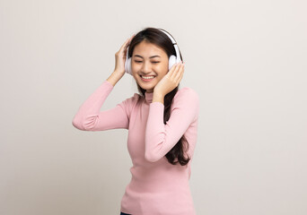 Cheerful asian female teenager listen to the music with white headphone on isolated. Beautiful young woman in pink shirt hand touch a wireless headphone having fun with the music in  room.