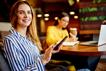 Cheerful woman messaging using smartphone in lounge