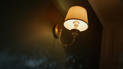 Beautiful sconce hanging on wall in dark room. Elegant lamp glowing in dark.