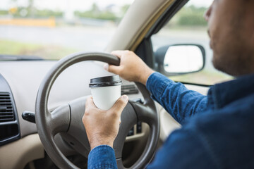 Young man drinking a cup of hot coffee while driving car to travel. Hands holding steering wheel.