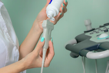 a doctor in a medical gown applies gel to an ultrasound machine for human organs.