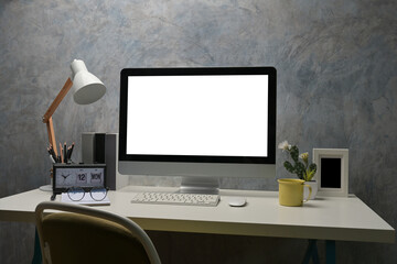 The white blank screen computer monitor on a working desk surrounded by various equipment.