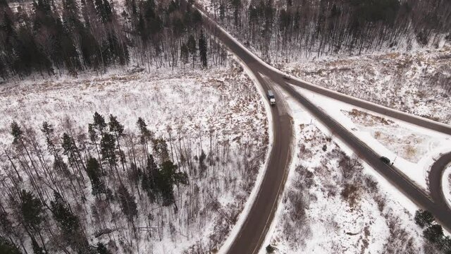 A fork on a suburban highway with driving cars in winter, aerial view. Highway panorama on a cloudy winter day, warm soft light. There is snow on the side of a multi-lane road. UHD 4K.