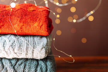 Three woolen sweaters of different colors on the background of garlands.