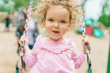 Happy little girl is playground having fun on swing