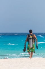 Latin man with a scuba tank fins mask preparing to dive walking on the beach.
