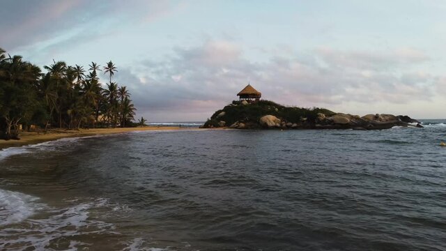 Aerial view of two girls on a beach, a hut and palm trees in the middle of the Caribbean Sea in Tayrona National Natural Park, cabo san juan del guia Colombia, South America from a drone