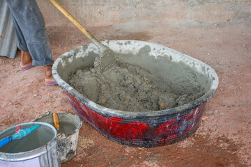 Construction worker manually mixing concrete in mixer tray.
