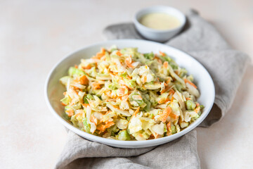 Coleslaw. Salad made of shredded white cabbage, grated carrot and rhubarb with orange mayonnaise dressing in white bowl, light background.