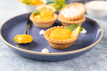 Obraz na płótnie Canvas Lemon curd mini tarts decorated with mint and lemon slices on blue ceramic plate.