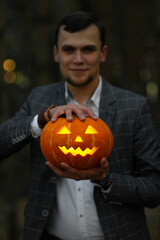 Smiling man in suit holds a carved glowing pumpkin lantern with a creepy face. Horrible symbol of Halloween - Jack-o-lantern