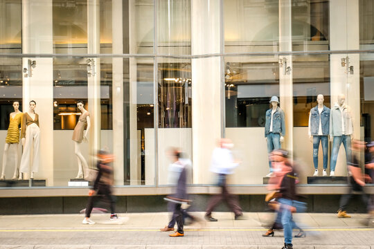 Motion blurred people walking past retail shop window on London high street