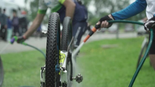 An athlete washes his mountain bike under a tap of water from a hose