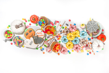 Set of various classic Halloween treats on white background. Selection assortment traditional cookies, gingerbread, candy, sweets and decor pumpkins. Trick or treat concept, top view copy space