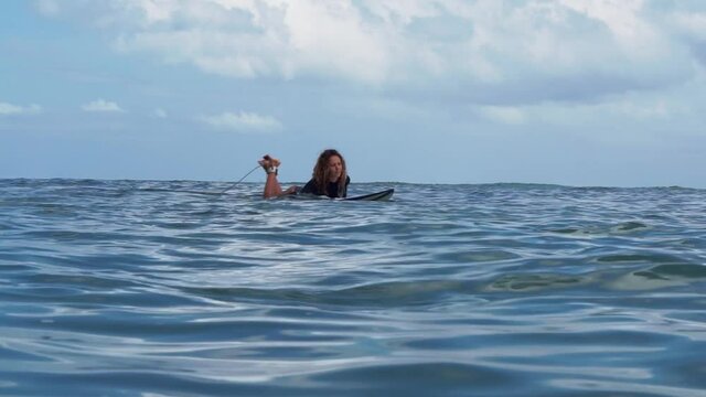 Portrait of surfer girl on white surf board in blue ocean pictured from the water in Bali