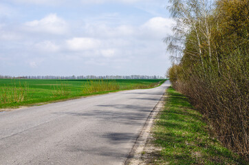 An empty asphalt road goes into the distance. The track is located outside the city. Shot in early spring