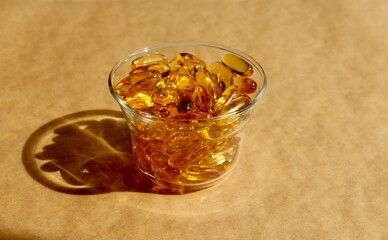 Capsules in a transparent glass bowl on craft background. Healthy lifestyle, naturopathy, food supplements and vitamins concept