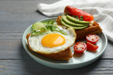 Delicious Belgian waffle with fried egg, arugula and vegetables on grey wooden table, closeup